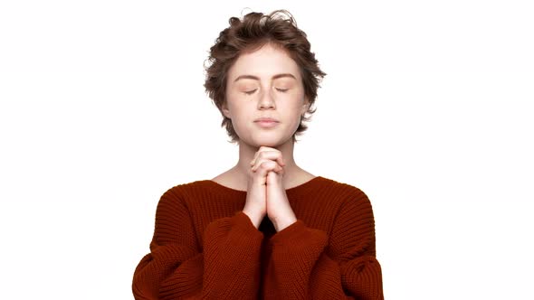 Portrait of Brunette Woman Keeping Hands in Praying Wishing Luck with Closed Eyes Over White alt