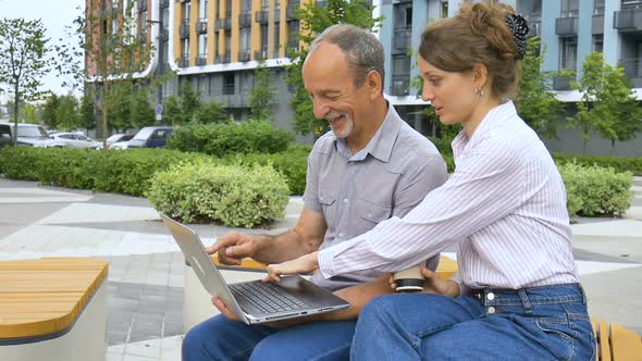 Young Employee is Teaching Her Older Colleague How to Use Laptop and Corporate Software Sitting on alt