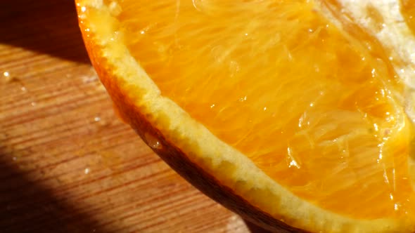 Macro shot on a ripe orange fruit slice with juice dripping off of it in the sunlight on a cutting b alt