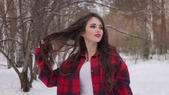 Young Woman with Wavy Hair Standing and Touching Face in Winter Forest