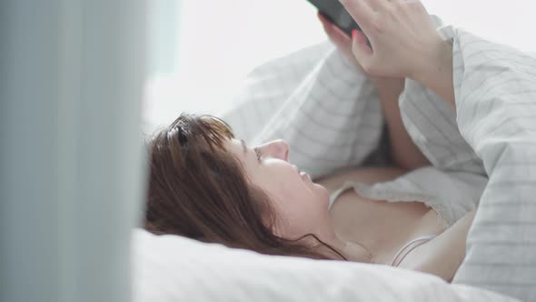 Pretty Brunette Woman Puts Head on a Pillow in the Bed in the Morning and Uses the Phone Reading