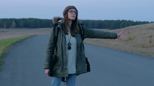 Female Tourist Can't Catch a Car in Evening Walking Along the Road alt