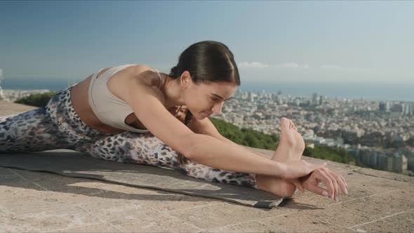 Woman Doing Twisted Head To Knee Pose Outdoors. Trainer Exercising in City alt