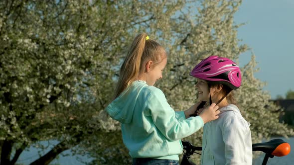 Children learn to ride bicycle in a park on spring day. Teenager girl helping preschooler girl