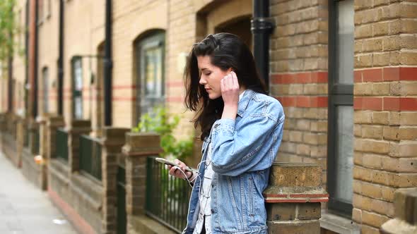 Beautiful young woman listening at music in the city alt