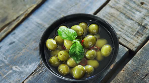 Bowl of green olives in vinegar garnished with herb alt