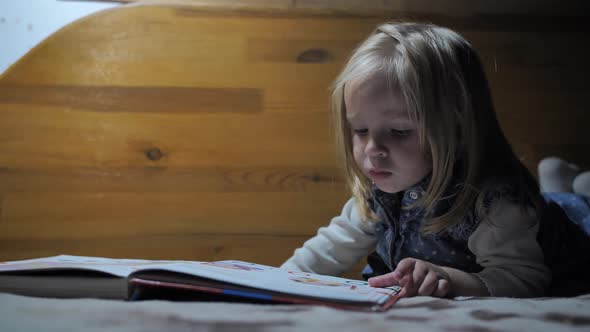 Little Girl Leafing Through Pages of a Book By the Light of a Lamp alt