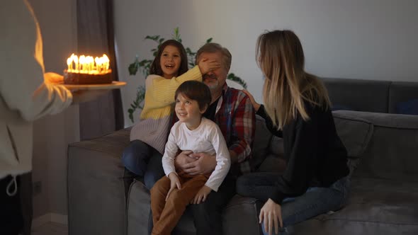 Happy Grandfather with Closed Eyes Blowing Candles on Birthday Cake with His Family alt