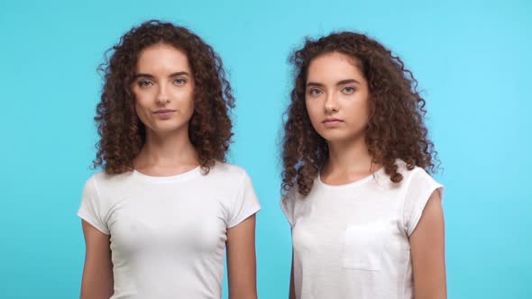 One Beautiful Caucasian Twin with Curly Hair Wearing White Tshirt Showing Ok While Another Removing alt