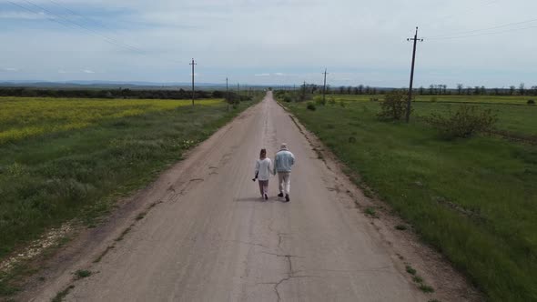 A Couple of Travelers Walk Along an Empty Road Holding Hands