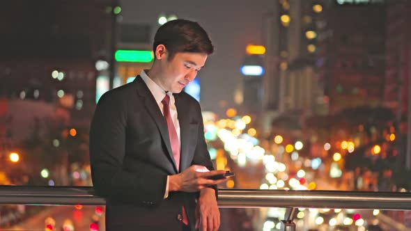 Asian businessman working by using moblie phone chat with colleagues team at night in city. alt