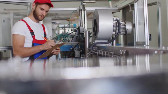 Young Factory Man in Uniform Making Notes on Clipboard at Water Production Factory