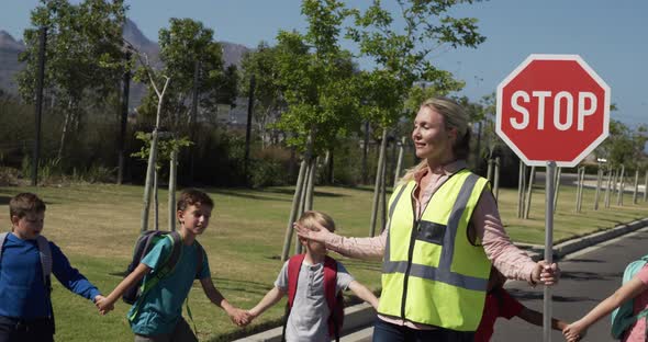 Woman with Hi-vest holding stop sign while group of kids cross the road alt