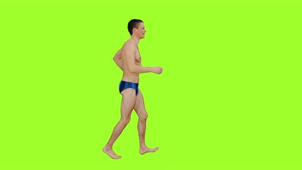 Young Man in Swim Trunks Jogging on Green Background