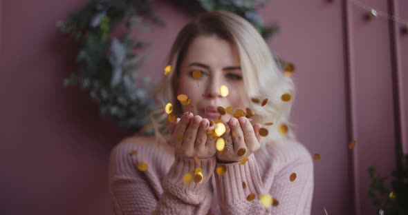 Beautiful Woman in Sweater Blows Shiny Confetti From Her Hands To the Camera in Slow Motion alt