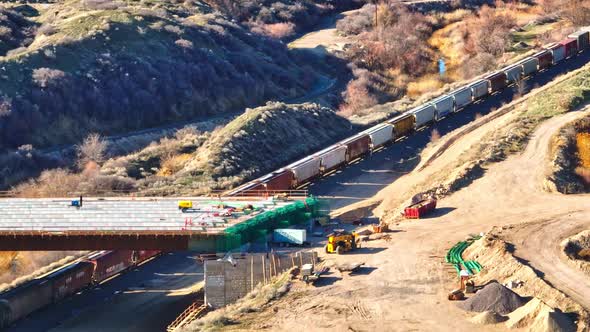 Aerial - Train Passing Below a Bridge Construction in Bluffdale Utah, Tracking Telephoto Lens alt