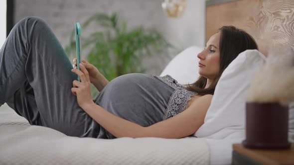 Side View Portrait of Young Beautiful Pregnant Woman Surfing Internet on Tablet in Slow Motion alt