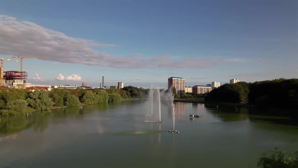 Drone flying backwards close to trees on island in pond, Pildammsparken Malmö, Sweden alt