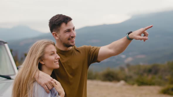 Young Traveler Couple on Road Trip in Mountains Standing Near Car