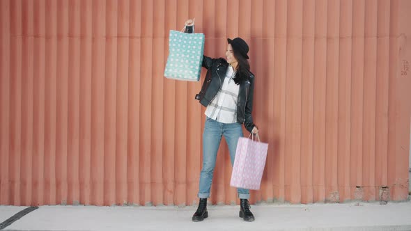 Portrait of Cute Girl Holding Shopping Bags Smiling Standing Alone on Wall Background alt