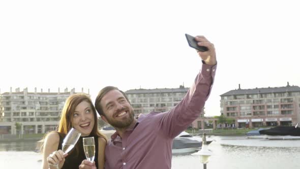 Couple holding champgne glasses and posing for selfie outdoors