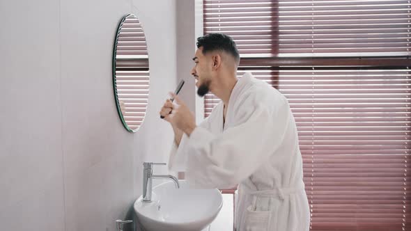 Side View Carefree Funny Arabic Hispanic Indian Man Bearded Guy in White Bathrobe Standing at Home alt