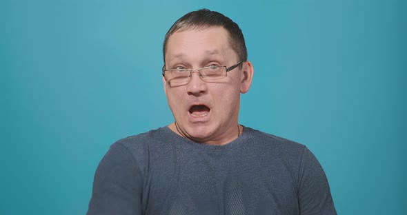 Man in Glasses and Grey T-shirt Sneezes Into Upper Sleeve alt