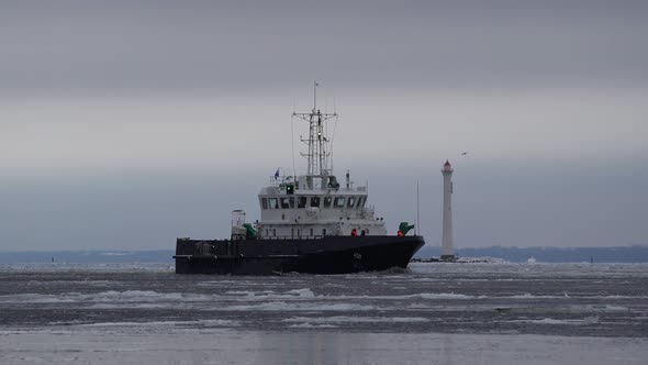 A Small Vessel Sails Against Background of a Lighthouse