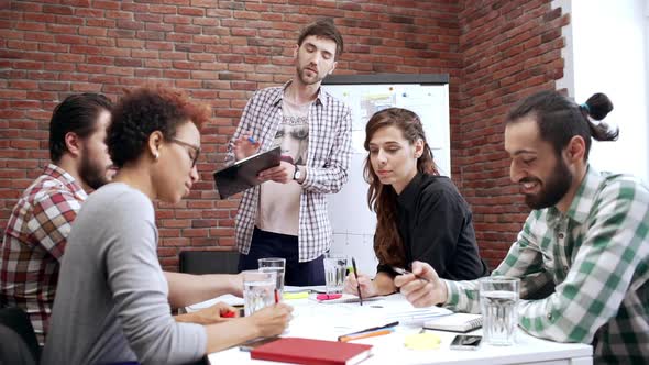 Team Lead Standing Next to Table with Teammates Coworkers Discuss Work Business Meeting of People in
