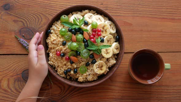 Wholegrain Oatmeal porridge with fresh berries, fruits, nuts, mint leaves in child hands. alt