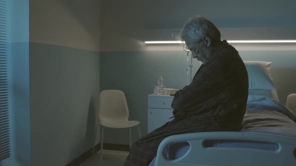 Sad hopeless senior sitting in a hospital bed alone