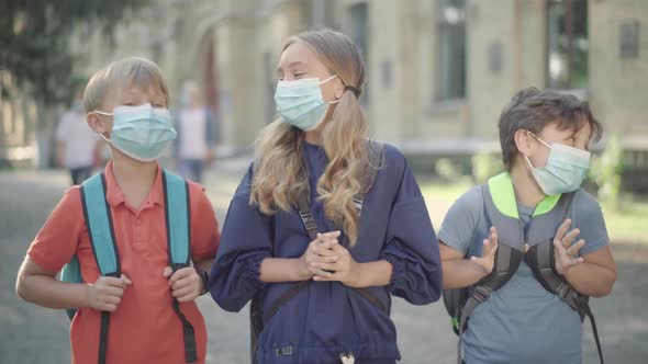 Positive Caucasian Pupils in Face Masks Posing Outdoors As Blurred High-school Students Passing at alt