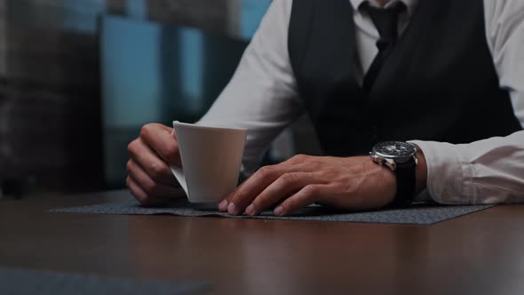 Business Man Sitting at the Table in the Office Drinks Coffee From a White Cup alt