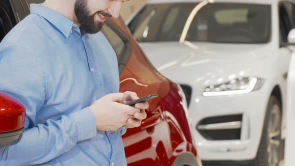 Cropped Shot of a Happy Man Using Smart Phone at Car Dealership alt