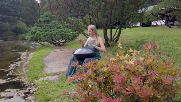 Popular Modern Hang Musical Instrument in the Hands of a Beautiful Blonde in Park alt