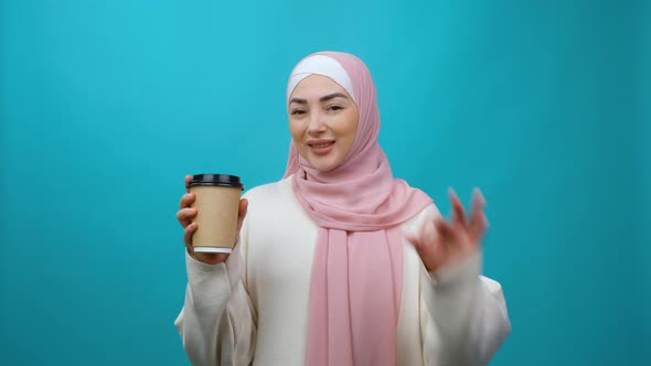Smiling Young Muslim Woman in Hijab Isolated Hold Paper Cup of Coffee or Tea Showing Ok Okay