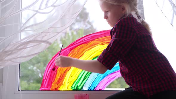 Girl Painting Rainbow on Window During Covid19 Quarantine at Home alt