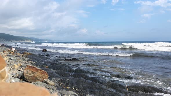 An empty beach on the sea, waves fall on a rocky shore against a background of mountains.