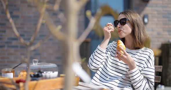 Woman Having a Breakfast with Croissants and Coffee Outdoors alt