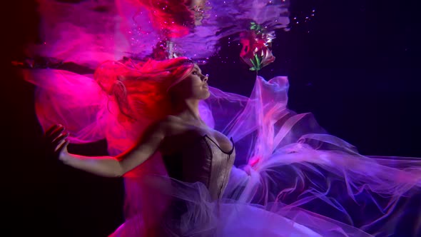 a Woman with Red Hair in a Corset Floats in the Dark Under Water with a Translucent Fabric. Side alt