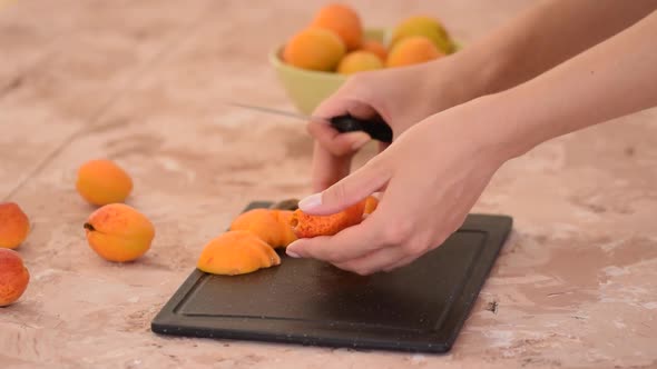 Female hands cutting fresh sweet apricot. Apricots slices on kitchen table.