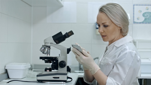 Scientist working with microscopes and smartphone in chemical lab