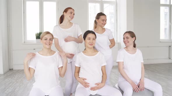 Asian and European Pregnant Women Sit on Fitness Mat Having Conversation