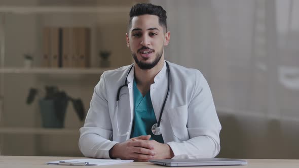Cheerful Smiling Young Man General Practitioner Doctor with Stethoscope Talking at Camera Explaining alt