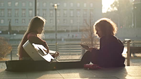 Teenage Girls Sit on the Embankment of the City