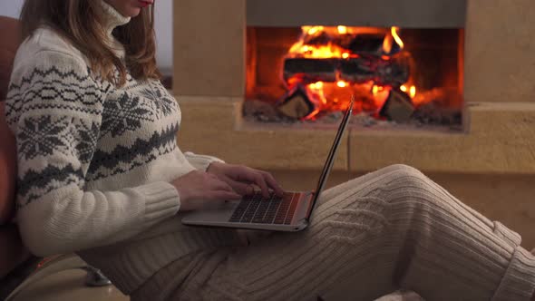 Young Freelancer Woman and Her Cat Sits at the Floor with a Laptop on the Fireplace Background alt