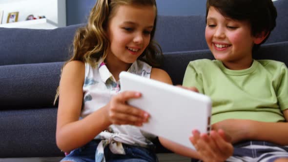Siblings using digital tablet in living room alt