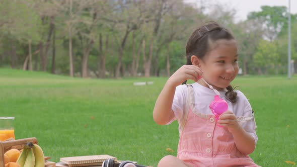 Happy little girl kid blowing soap bubbles playing alone in the park, Child having fun outdoor.  alt