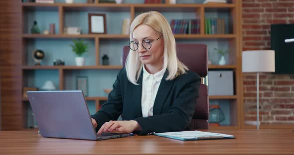 Beautiful Blonde Businesswoman in Business Clothes Works at the Computer in the Office alt