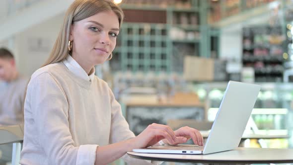 Laptop Use By Young Woman Smiling at Camera in Cafe alt